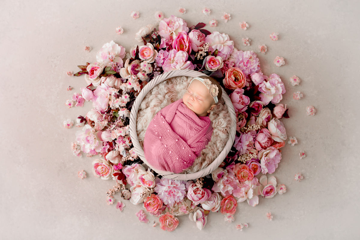 Newborn-Fotografie in Dillingen – Baby im rosa Wickeltuch auf Blumenbett